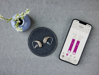 Oticon Intent hearing aids lying next to a smartphone with the Oticon app